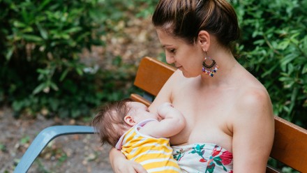 woman breastfeeding her baby on a park bench, women who love their postpartum bodies