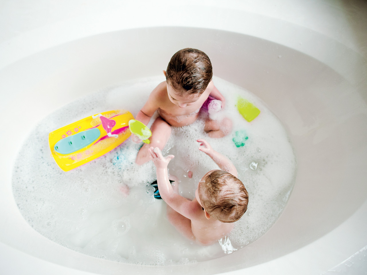 two babies in the bath with tub toys