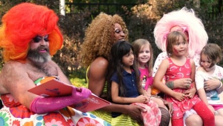 A drag queen reading a book surrounded by kids
