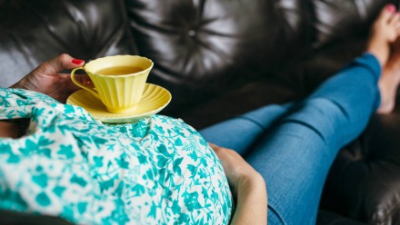 A pregnant woman lying on the couch with cup of tea on her belly