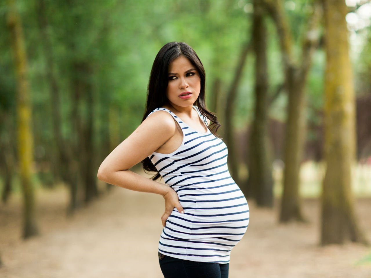 annoyed pregnant woman stands outside in park