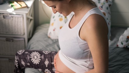 Pregnant woman sitting in bed looking down at her belly