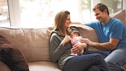 New parents sit on the couch with their newborn
