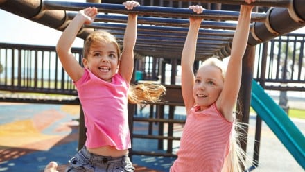 two little girls swing from bars at playground