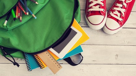 green backpack with school supplies spilling out of it with red converse shoes on a wooden background, how to get kids with ADHD organized for school