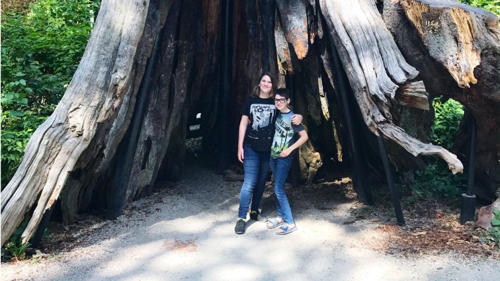 Trans daughter and sibling brother smiling for a photo in front of a tree 