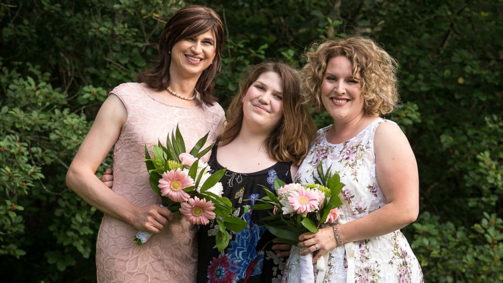 transgender wife and wife smiling holding a bouquet with transgender daughter in the middle