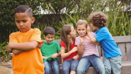 group of kids whispering to each other and excluding one boy out of the group