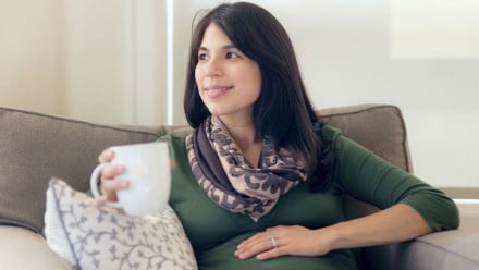 woman enjoying a cup of coffee while holding her pregnant belly
