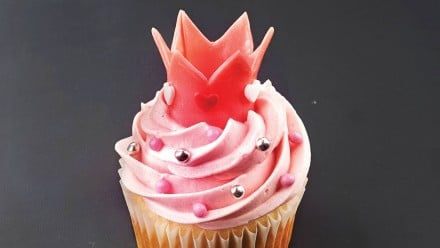 A cupcake decorated with pink icing and a pink crown