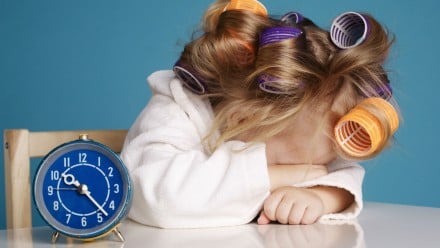 little girl sleeping at a table with an alarm clock in front of her