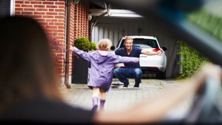 little girl running to her father with arms open, as mother watches after dropping the daughter off.