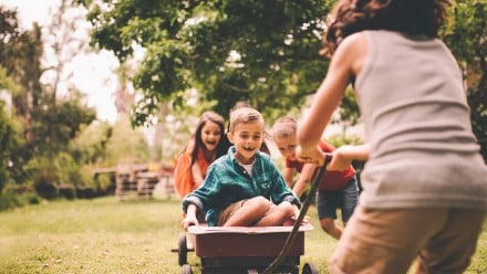 Kids playing outside in a wagon while another kid pulls them