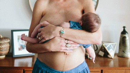 Woman breastfeeding her baby while showing her mummy tummy