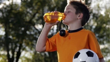 Little boy holding a soccer ball and drinking out of a water bottle