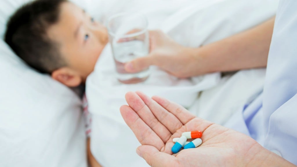 A little boy lies in a hospital bed as a doctor gives him pills