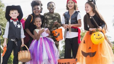 A multi-ethnic group of seven children wearing halloween costumes. They are mixed ages, from 3 to 10 years old, ready to go trick or treating.