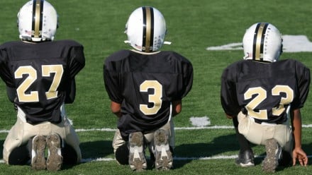 young kids (football players) sitting and kneeling on the sidelines