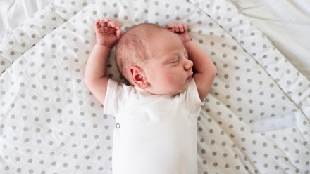 Cute little newborn baby boy lying on bed, sleeping on a white and grey polka dot blanket, hands up.