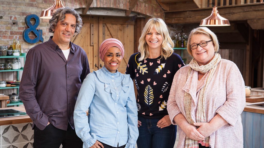 Promo image for the Big family cooking showdown. Shwos four people standing in a kitchen and smiling