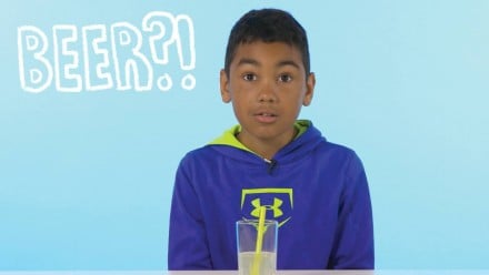 A little boy looking confused next to a glass of liquid
