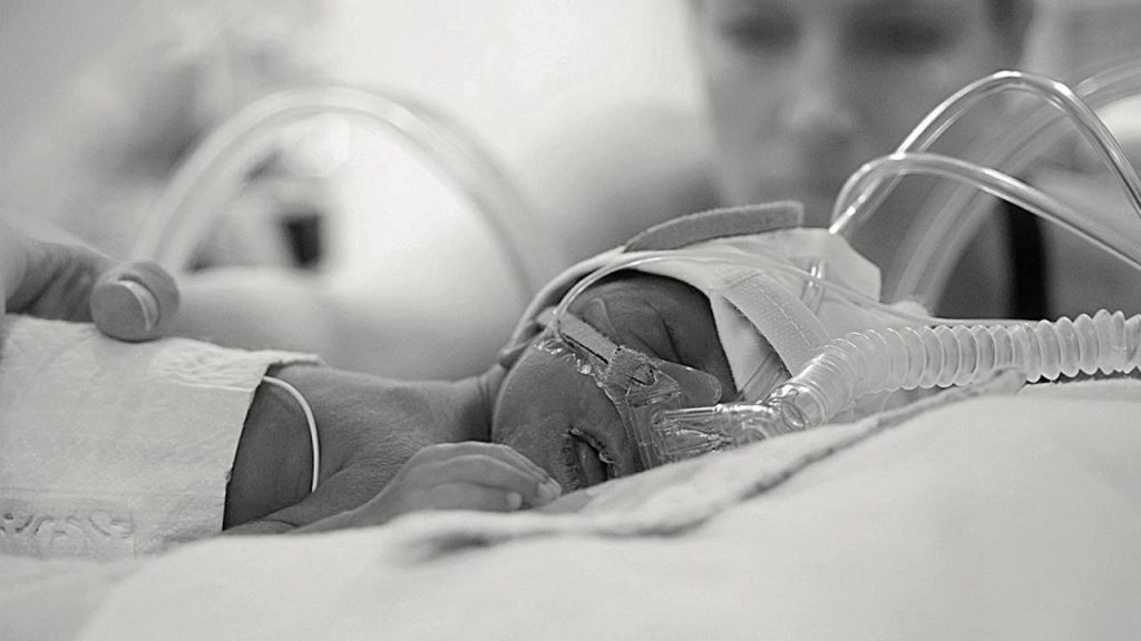 A mom reaching in to touch her preemie in the NICU