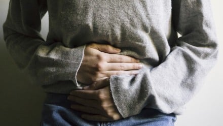 Woman wearing a grey sweater holding her stomach