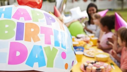 kids sitting at a birthday table, huge balloon that says happy birthday is the centre focus