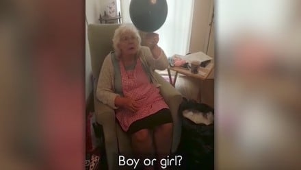 Screenshot of a video where Grandma reaches to pop a balloon for a gender reveal