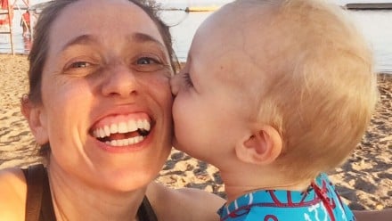 Toddler son gives his mom a kiss on the cheek as they sit on the beach