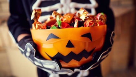 child dressed as a skeleton holding a pumpkin bowl of Halloween candy