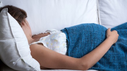 Pregnant woman sleeping on a white couch with a blue woven blanket