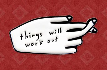 White enamel pin saying things will work out with fingers crossed