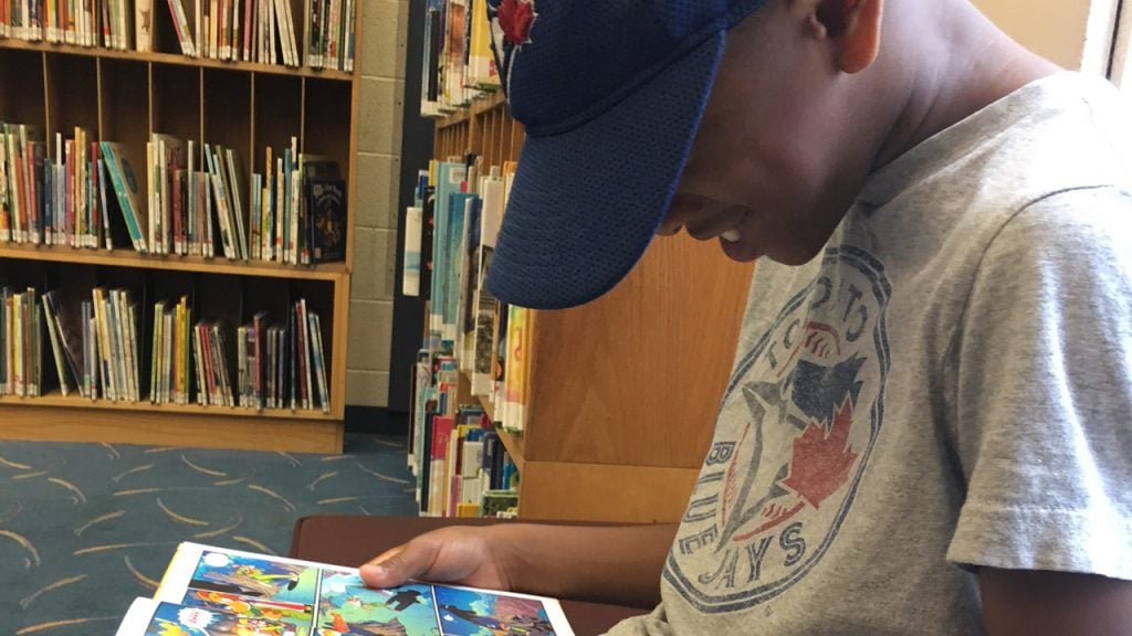 Little boy wearing Blue Jays shirt reading graphic novel in a library