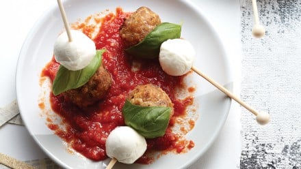plate of homemade meatballs on skewers with bocconcini and basil in marinara sauce