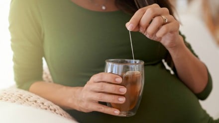 A pregnant woman dunking a teabag in a mug