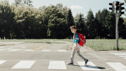 Boy wearing a backpack walks across the street alone