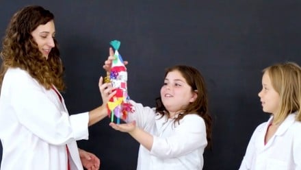 A woman handing a bottle rocket to a young girl with brown hair