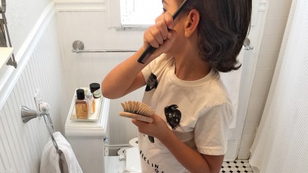 Kid brushing their hair in front of the bathroom mirror