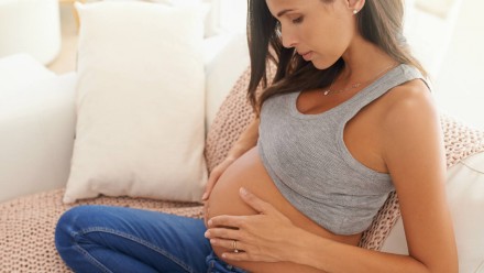 A pregnant woman sitting on the couch and holding her belly
