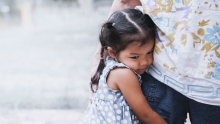 A young girl hugs her parent's leg.