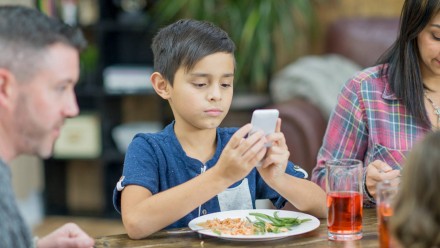 A kid sitting at the dinner table playing on a phone