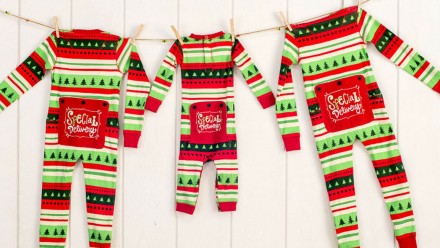 Three matching Christmas onesies in adult, kid and infant sizes.