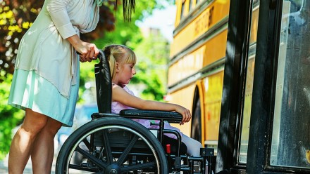 Woman pushing young girl in a wheelchair to the school bus