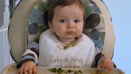 Baby in a high chair with spinach all over his face and bib