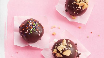 Pink sheet with three chocolate balls topped with sprinkles and crushed nuts