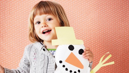 Little girl holding a snowman made from paper plates and cotton balls