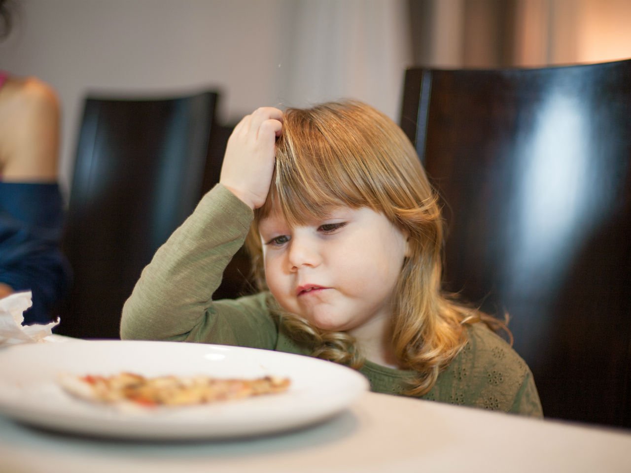 A young girl pouts at a plate of food on the table in front of her