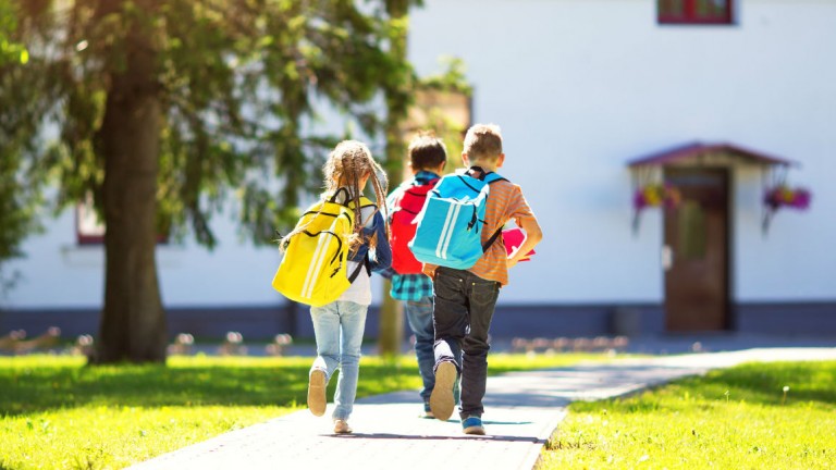 Photo of children with backpacks, walking towards a school building