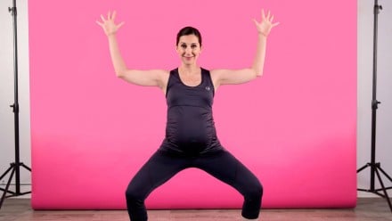 A pregnant woman doing a squat with her arms in the air